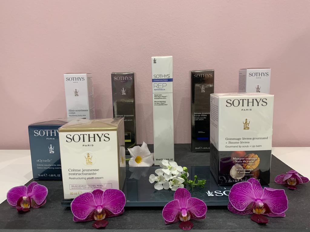 SOTHYS Pflegeprodukte, dekoriert mit weißen Orchideen vor einer rosa Wand